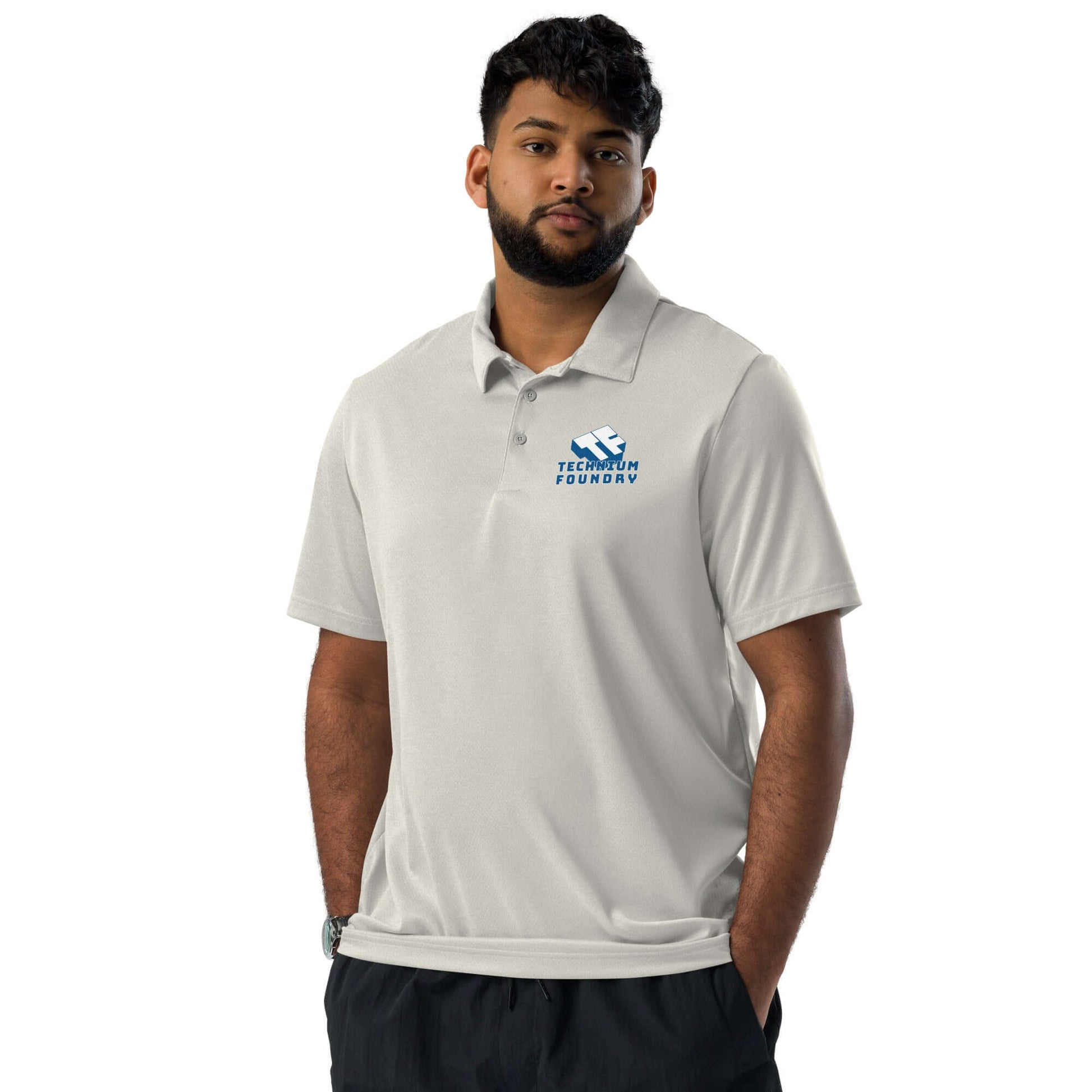 Man wearing gray polo shirt with Technium Foundry logo, hands in pockets, standing against white background.