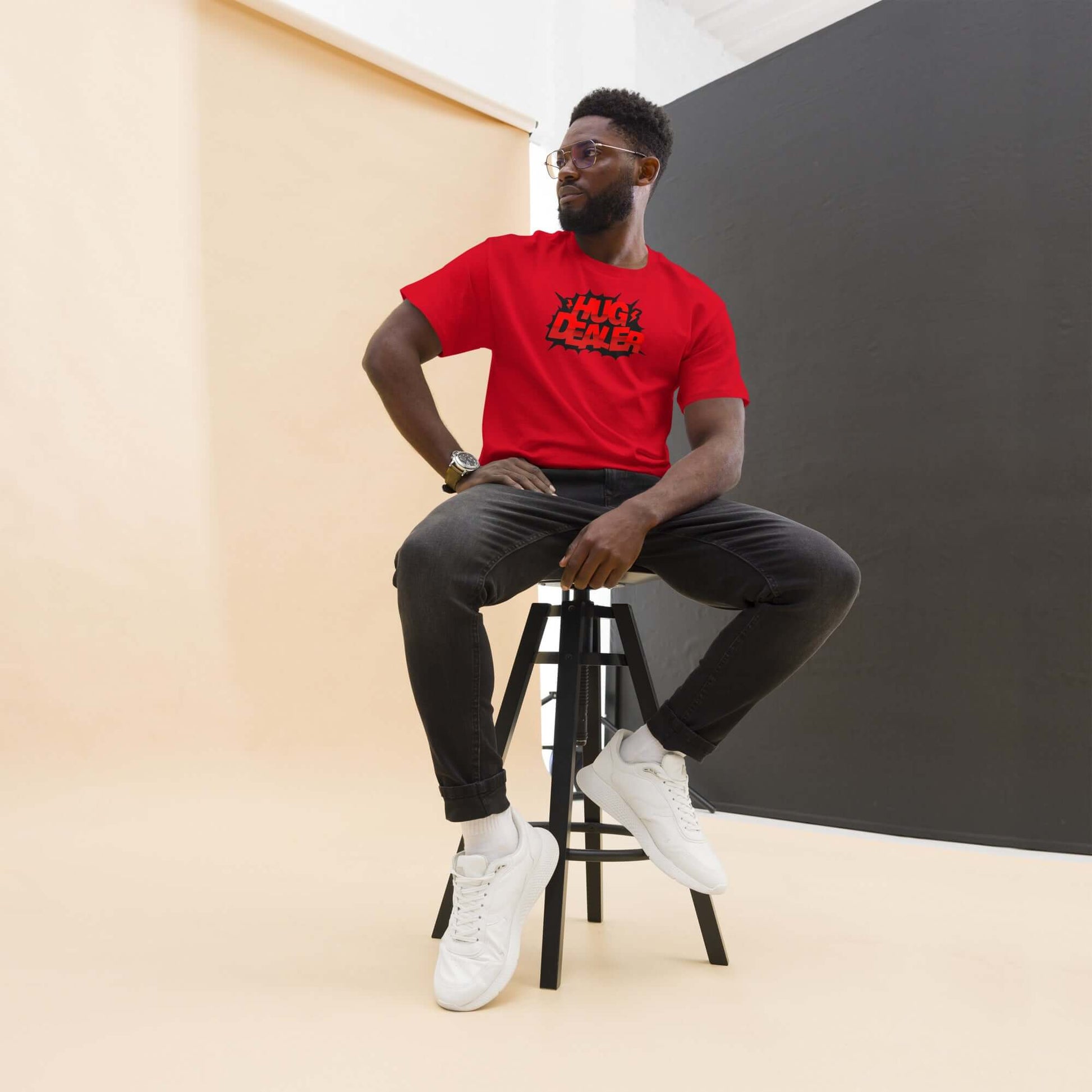 Man wearing red 'Hug Dealer' t-shirt with comic book design, seated on stool, showcasing bold style in modern studio setting.