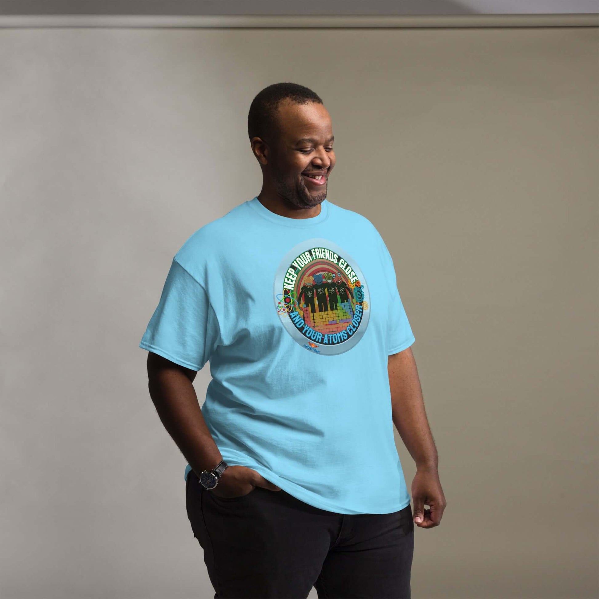 Man wearing "Keep Your Friends Close and Your Atoms Closer" tee with retro atomic design against cityscape backdrop.