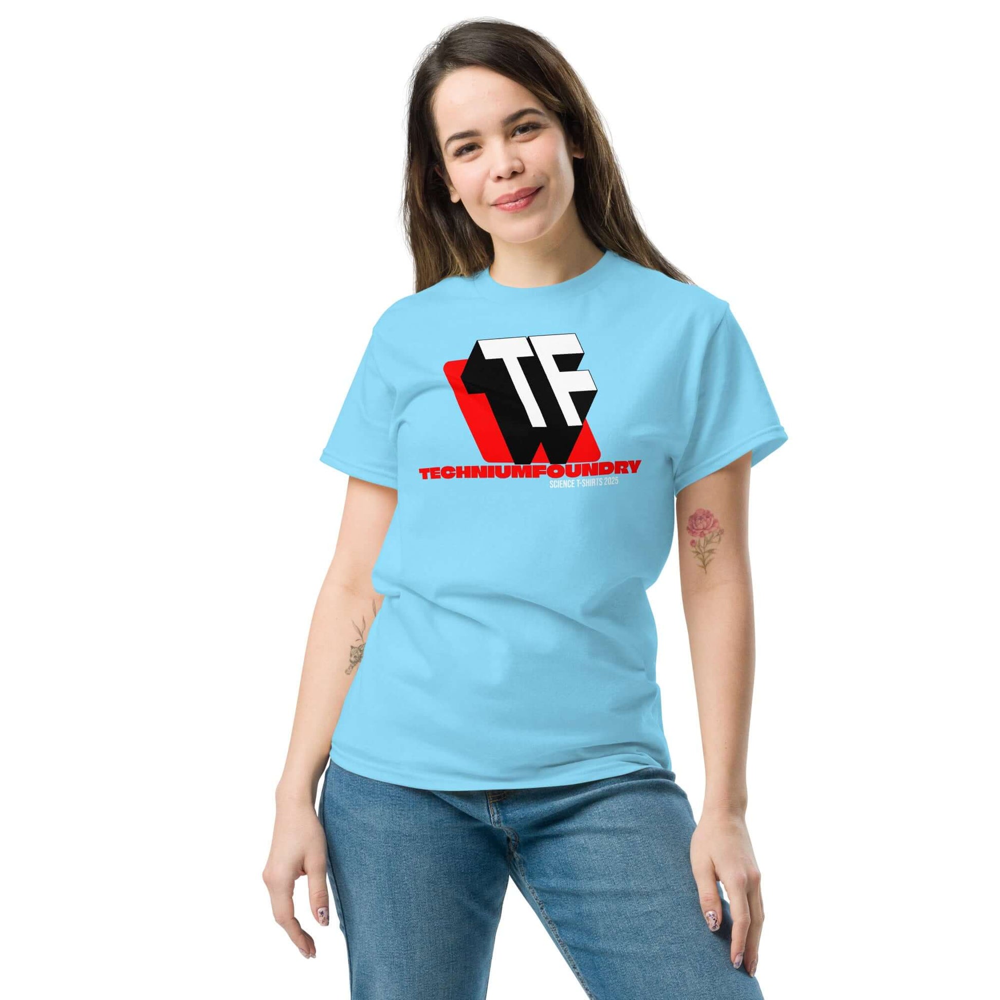 Woman wearing blue T-shirt with bold TF monogram and Technium Foundry logo, featuring red accents and geometric design.