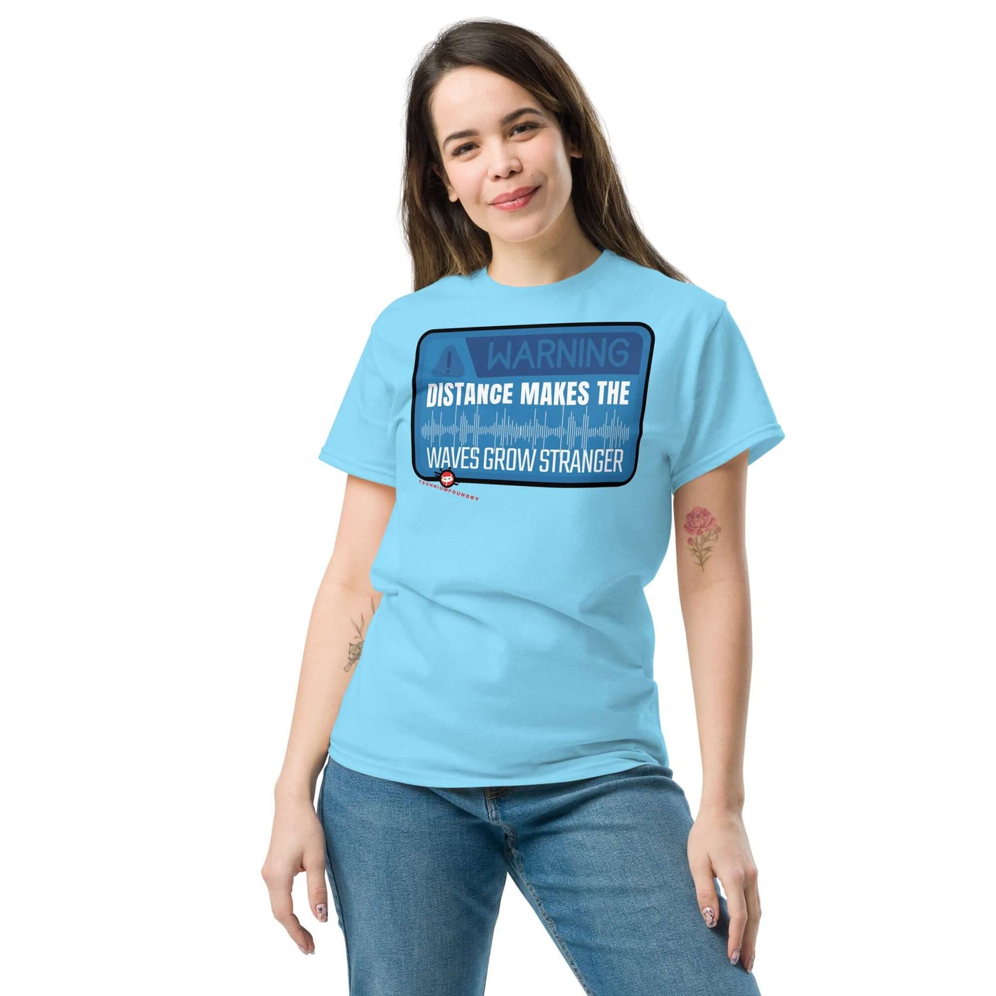 Person wearing a light blue "Warning: Distance Makes the Waves Grow Stronger" T-shirt, perfect for science enthusiasts and quantum apparel lovers.