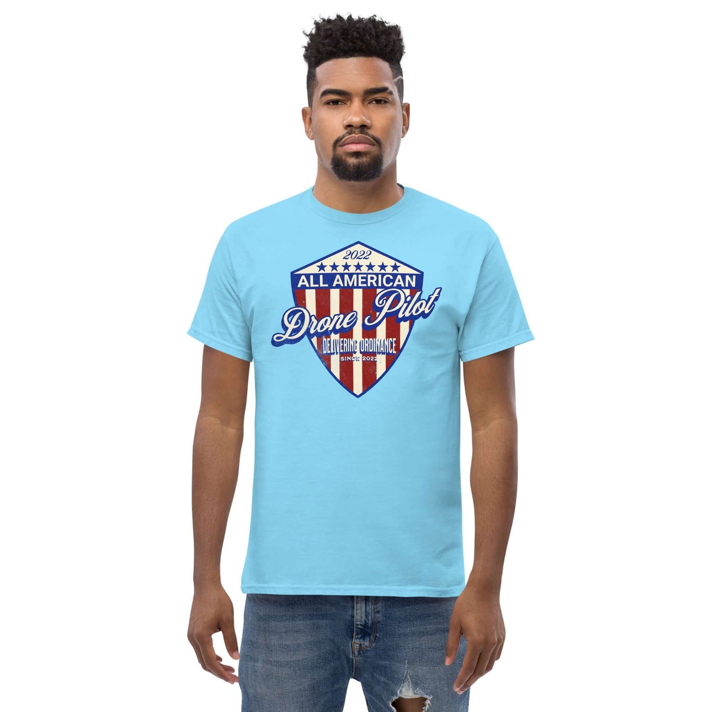 Man wearing '2022 All American Drone Pilot Champion' t-shirt with patriotic shield design on light blue fabric.