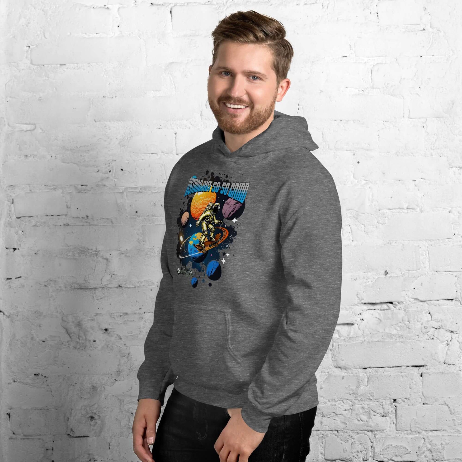 Man wearing gray hoodie with astronaut skateboarding design against a white brick wall.