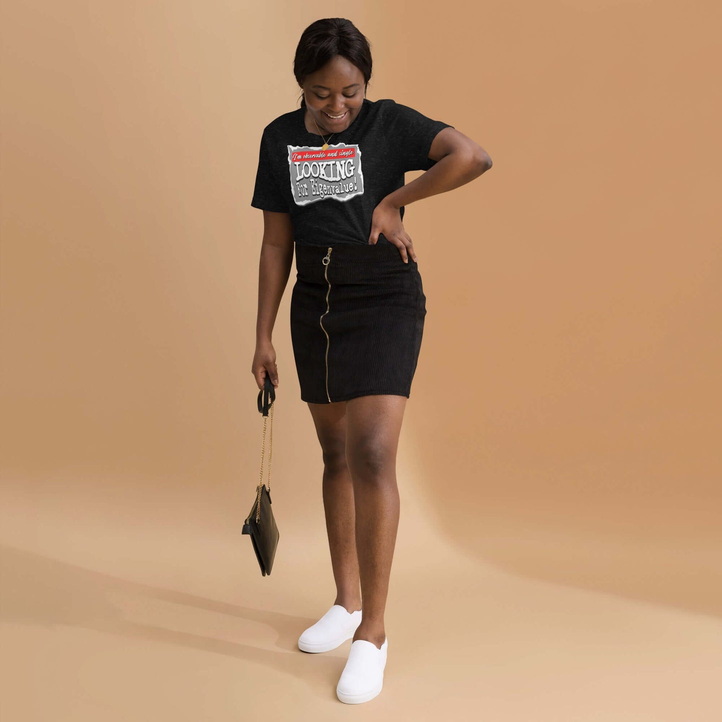 Woman in black 'Observable and Single' t-shirt, smiling while holding a purse, wearing a skirt and white sneakers.