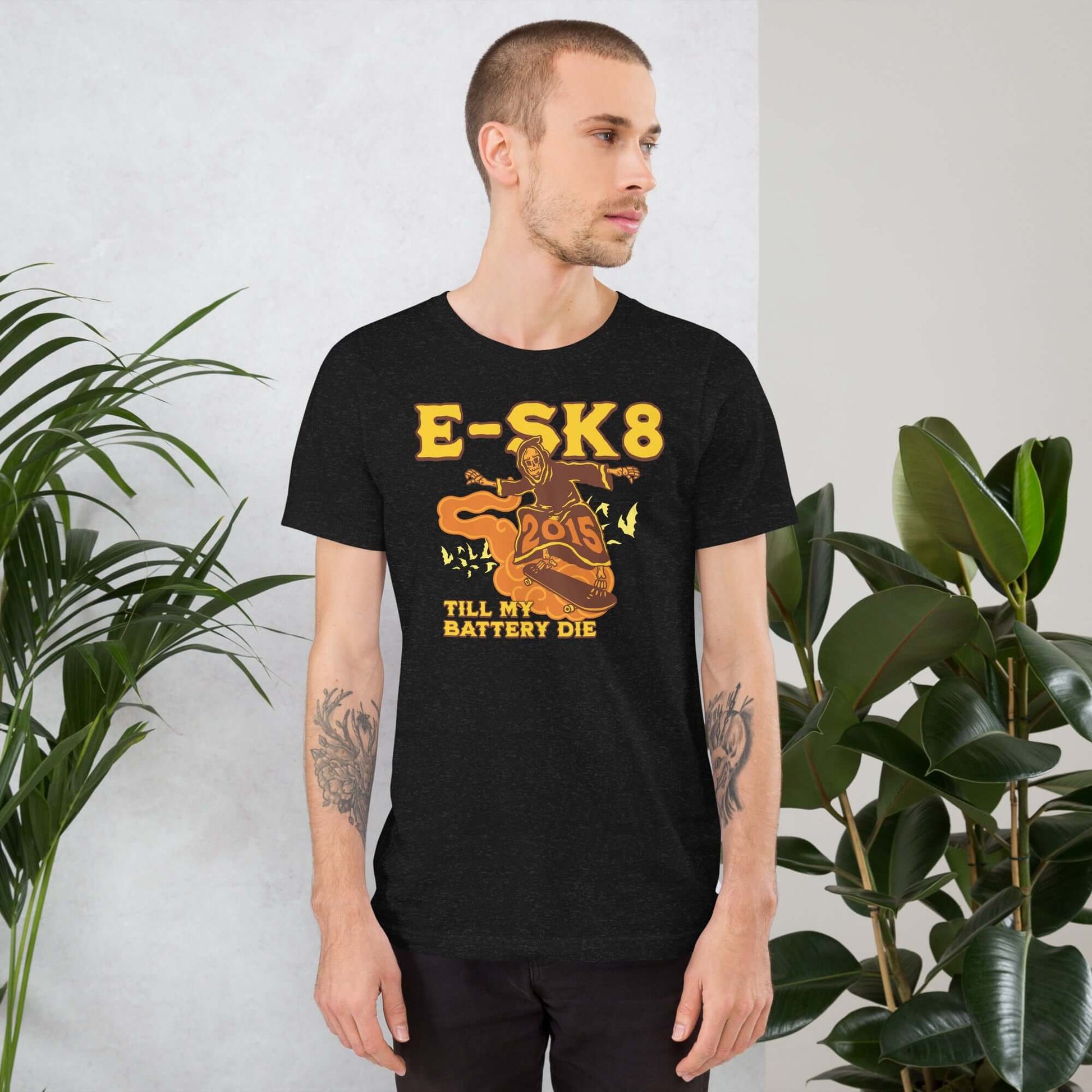 Man wearing 'E-SK8 Till My Battery Dies' T-shirt with Grim Reaper design, standing by indoor plants