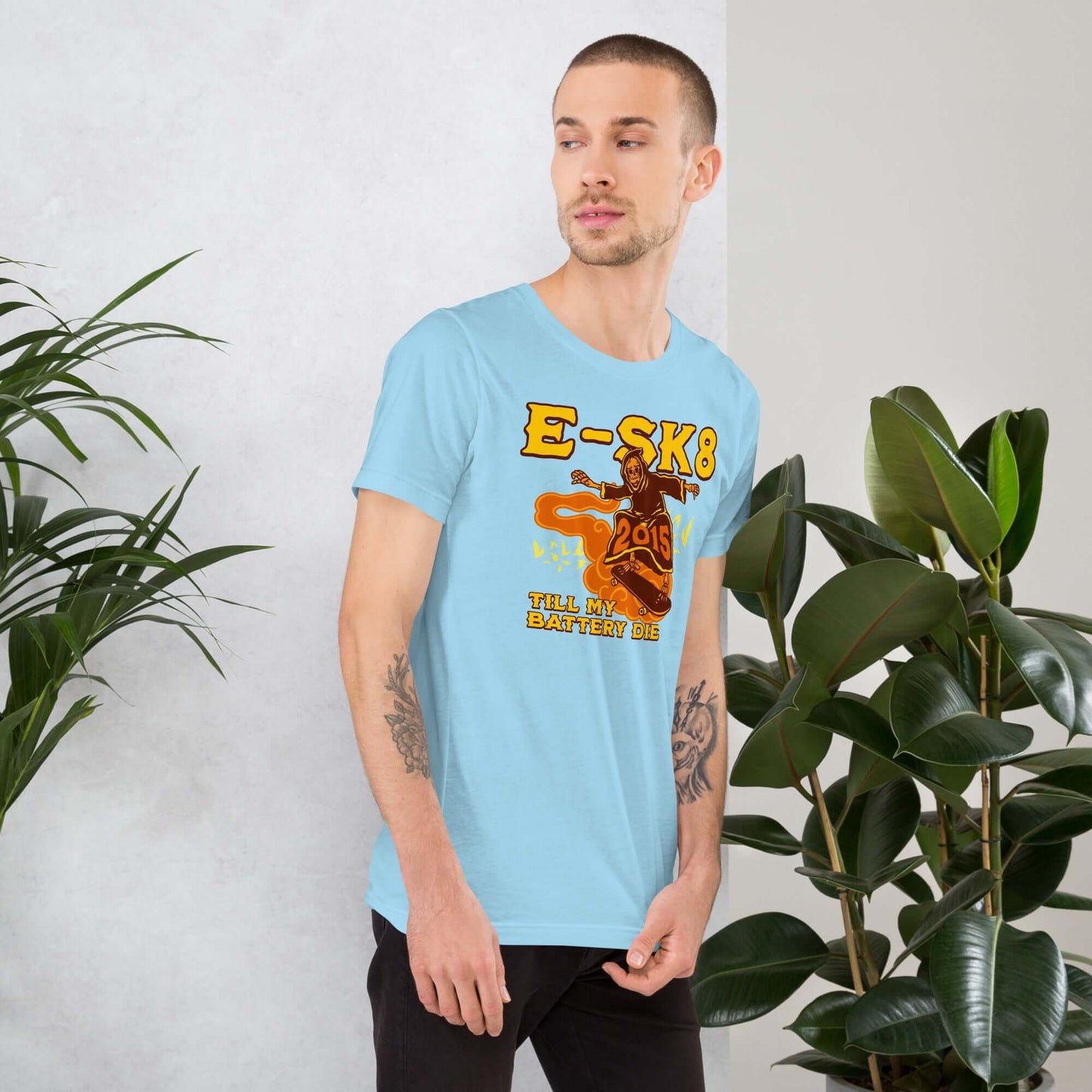 Man wearing E-SK8 Till My Battery Dies T-Shirt with Grim Reaper graphic, standing by plants.