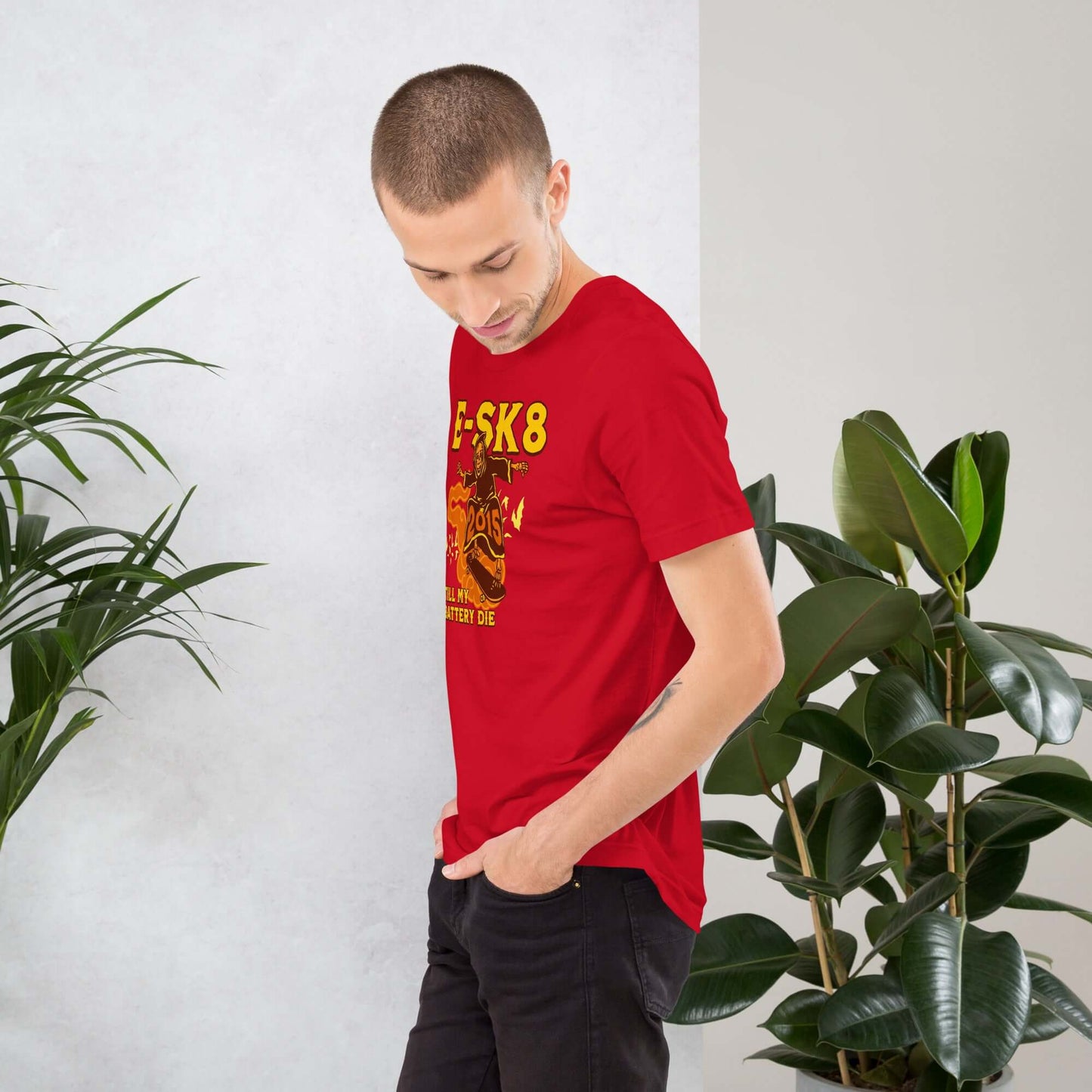 Man wearing red "E-SK8 Till My Battery Dies" T-shirt with Grim Reaper design, standing next to indoor plants.