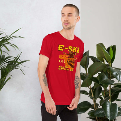 Man wearing red E-SK8 Till My Battery Dies T-Shirt featuring the Grim Reaper with an electric twist, standing near indoor plants.