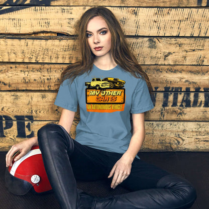 Woman wearing "My Other Car Is An Autonomous Vehicle" T-shirt, featuring vintage car design, sitting against wooden backdrop.