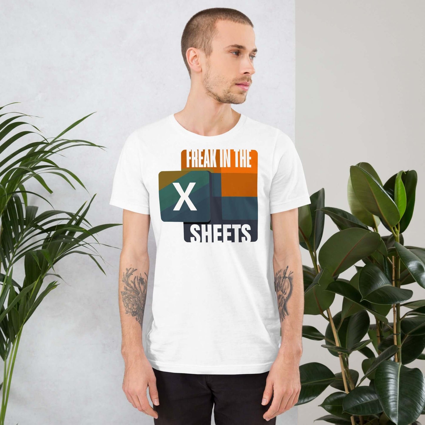 Man wearing 'Freak in the Sheets' Excel-themed t-shirt for data enthusiasts with a retro design, standing beside houseplants.