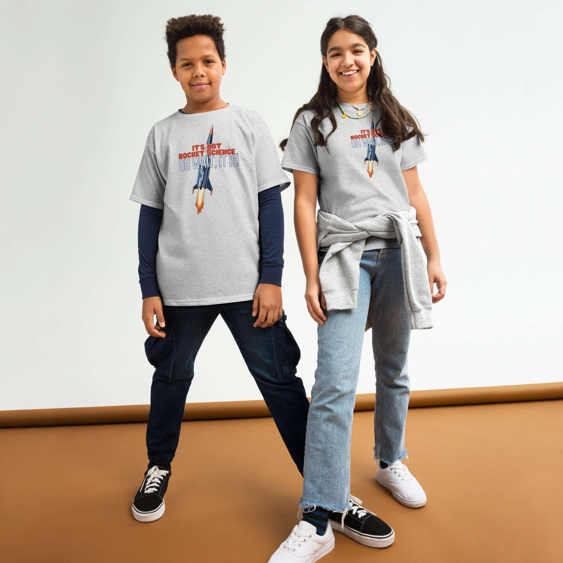 Two kids wearing "It's Not Rocket Science... Oh Wait, It Is!" tees with a rocket graphic, smiling and standing in casual outfits.